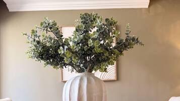 A wooden table with a large white vase containing green foliage.