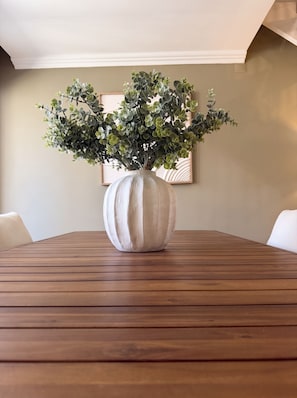 Une table en bois sur laquelle est posé un grand vase blanc contenant des feuilles vertes.