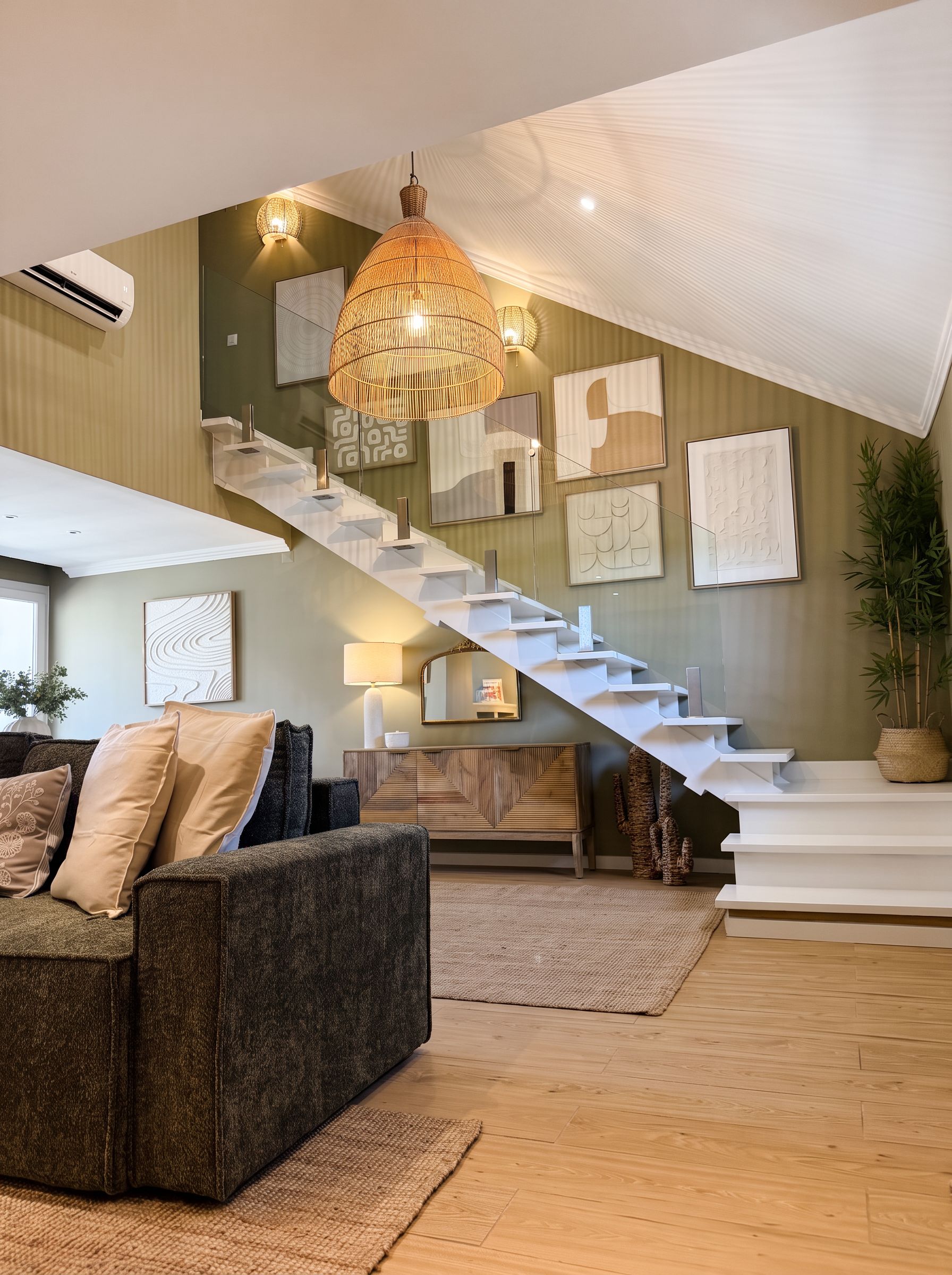 A modern living room with a staircase, a chandelier, and artwork on the walls.