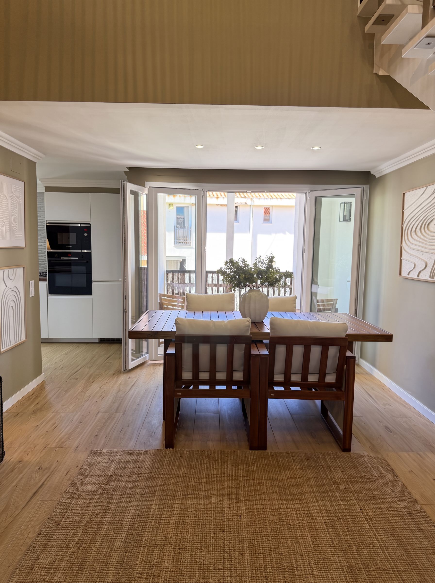 Un coin repas avec une table et des chaises, une cuisine équipée et une vue à travers une porte vitrée.