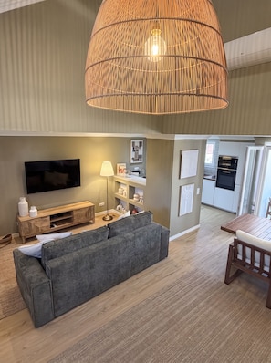 Un salon moderne avec un canapé gris, un téléviseur à écran plat, une lampe et un coin repas comprenant une table et des chaises en bois.