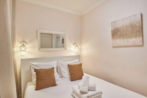A hotel room with a bed, two pillows, a folded towel, a wall-mounted mirror, and two wall sconces. - Lovely apartment with AC - Center of Paris (Paris)