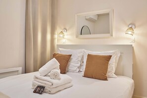 Une chambre d’hôtel avec un lit bien fait, un miroir au-dessus de la tête de lit et des lampes fixées au mur.