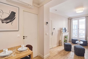 A room with a dining table set for two, a fireplace with a mirror above it, and a large window with curtains. - Lovely apartment with AC - Center of Paris (Paris)