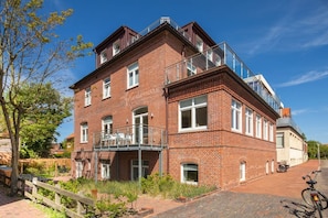 Ein mehrstöckiges Backsteingebäude mit einem Balkon und einem Fahrrad davor, bewölkter Himmel.