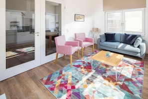 Ein Wohnzimmer mit einer Couch, Sesseln, einem Couchtisch und einem farbenfrohen Teppich.