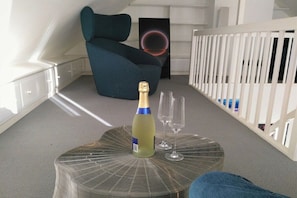 Ein Zimmer mit blauem Sessel, einem Tisch mit Flasche und Gläsern sowie einem weißen Babybett.