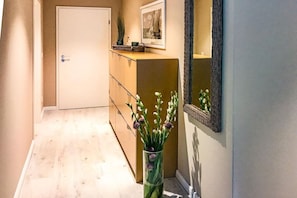 Ein Flur mit einer Tür, einem Holzschrank, einer Vase mit Blumen und einem Spiegel an der Wand.