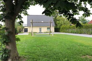 A residential property with a well-maintained lawn, a swing set, and a house with a tiled roof. - Holiday apartment with 1 bedroom (Grömitz - Lenste)