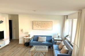 Ein modernes Wohnzimmer mit einem blauen Sofa, einem Glastisch und einem Flachbildfernseher.