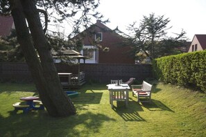 Ein Garten mit Tisch und Stühlen, einer kleinen Spielgegend und einem Hecken.