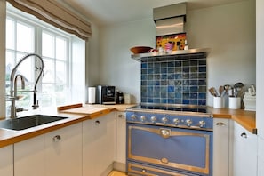 Una cocina con estufa moderna, un lavamanos y una ventana con cortinas.