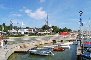A marina with boats docked, a pedestrian walkway, and buildings in the background. - Holiday apartment with 1 bedroom (Grömitz-Lenste)