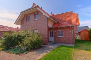 Een tweelaags bakstenen huis met een rode dakbedekking, een voordeur en een kleine voortuin met een pad dat naar de ingang leidt.