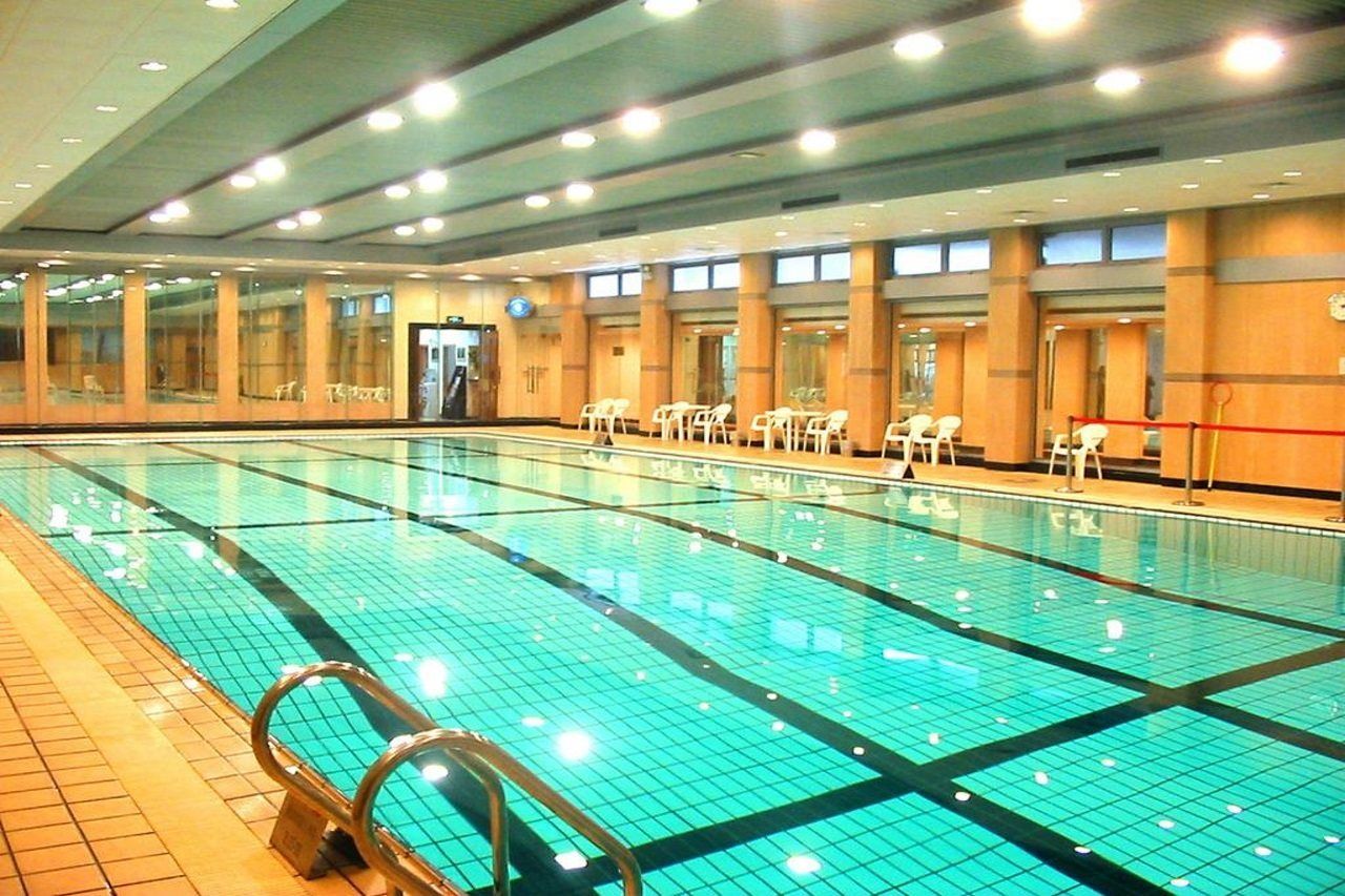A large indoor swimming pool with clear water, surrounded by chairs and a tiled floor.
