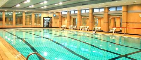 A large indoor swimming pool with clear water, surrounded by chairs and a tiled floor.