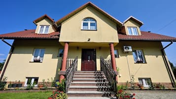 A two-story house with a brown door, a front porch with steps, and a red-tiled roof.