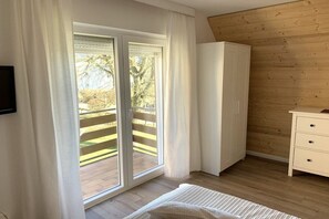 Une chambre avec un plancher en bois, un lit, une armoire et une porte-fenêtre coulissante donnant sur un espace extérieur.