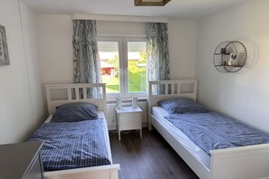 Une chambre avec deux lits simples, une petite table et une fenêtre avec des rideaux.