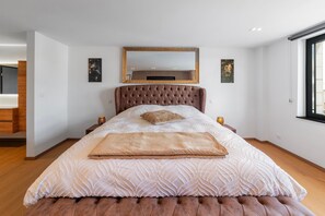 Ein Schlafzimmer mit einem großen Bett, einem gepolsterten Kopfteil und einem Spiegel darüber.