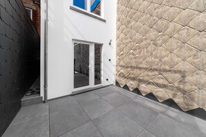 Ein modernes Gebäude mit weißer Fassade, einem Glastür-Eingang und einer gefliesten Terrasse.