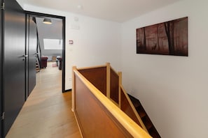 Een gang met een houten trap, een schilderij aan de muur en een deur naar een andere kamer.