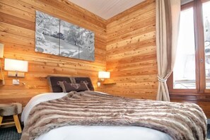 Um quarto com painéis de madeira, uma cama, duas luminárias fixadas na parede e uma janela com cortinas.