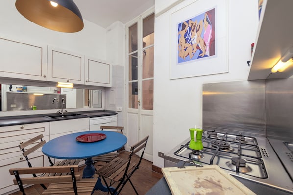 A modern kitchen with white cabinetry, a blue table, and a green kettle. - Bernini in Cavour (Roma)