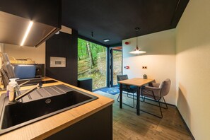 A modern kitchen with a sink, stove, and dining area with a table and chairs. - The Serene Escape – Olivenise Cabin (La Roche-en-Ardenne)