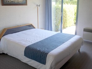 A neatly made bed with a headboard, a bedside table, and a window with curtains. - Hotel Les Dineux Village (Tremeur)