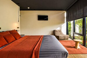 A modern bedroom with a large bed, a chair, and a small table. - The Blooming Refuge – Hydrangea Cabin (La Roche-en-Ardenne)