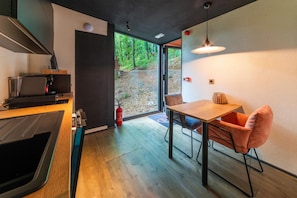 A modern kitchen with a dining area, a coffee machine, and a fire extinguisher. - The Blooming Refuge – Hydrangea Cabin (La Roche-en-Ardenne)