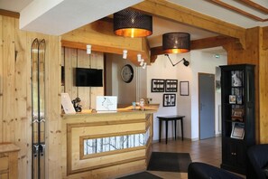 A reception area with wooden walls, a reception desk, a clock, framed pictures, and a black cabinet with framed photos. - Hôtel Restaurant De La Buffe (Autrans-Meaudre-en-Vercors)