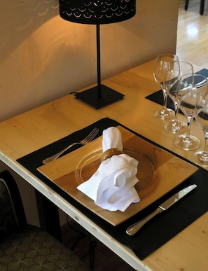 A table set with a wooden plate, a folded napkin, a fork, a knife, and a wine glass. - Hôtel Restaurant De La Buffe (Autrans-Meaudre-en-Vercors)