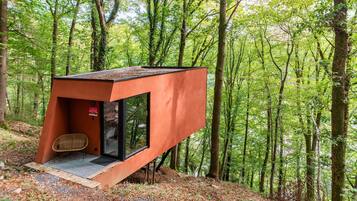 Uma estrutura moderna, vermelha, que lembra uma casa na árvore, com porta de vidro e uma pequena área de estar.