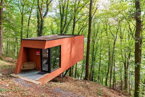 Una estructura moderna, de color vermell, semblant a una caseta d'arbri amb una porta de vidre i una petita zona de seients.