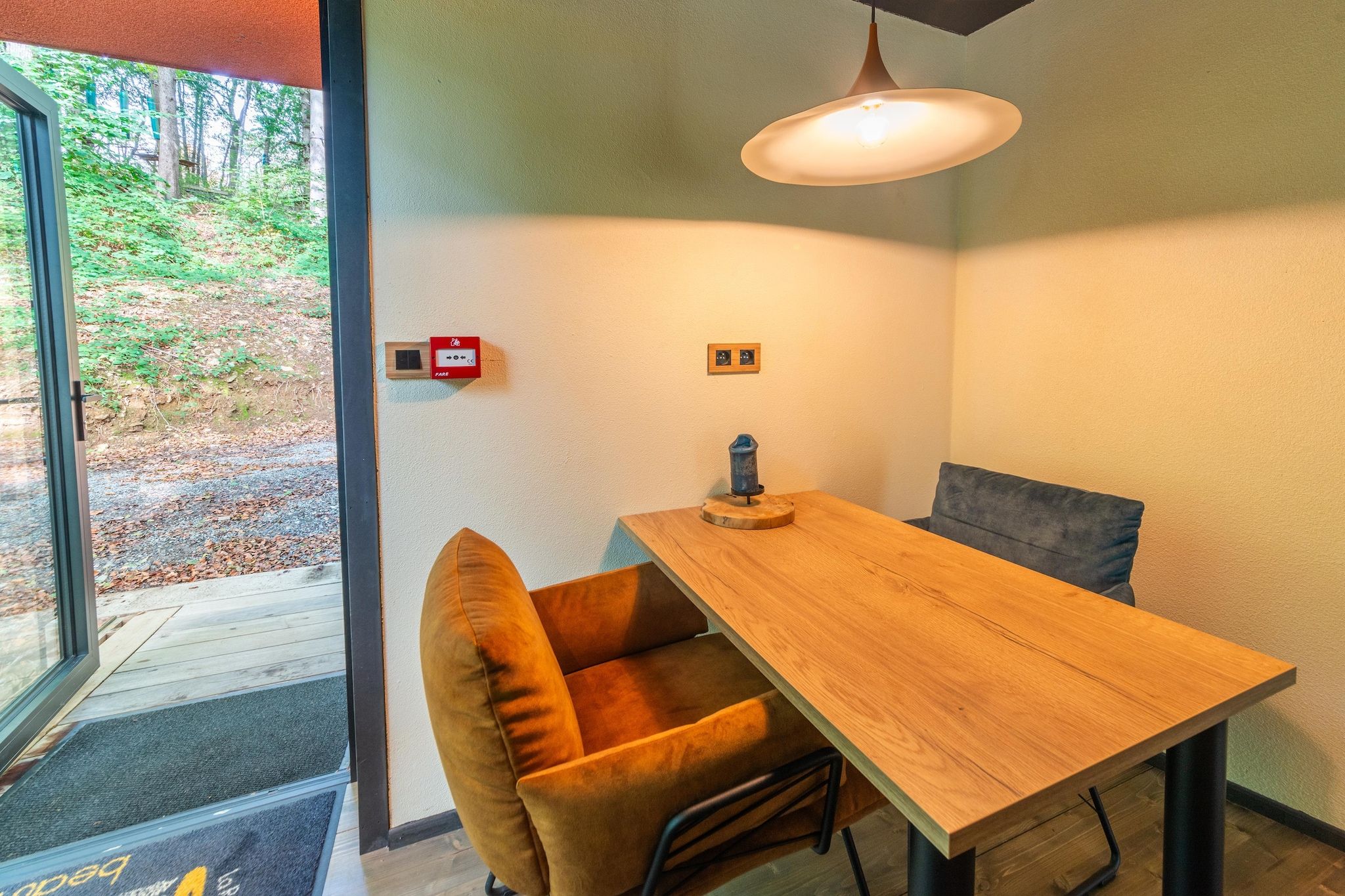 A dining area with a wooden table and two chairs, a pendant light, and a view of the outdoors through a glass door.