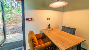 A dining area with a wooden table and two chairs, a pendant light, and a view of the outdoors through a glass door.