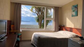 A hotel room with a bed, a desk, a chair, a TV, and a window with a view of a body of water and mountains.