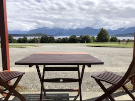 Un área de estar techada al aire libre con una mesa y dos sillas, con vista a un lago y montañas.