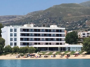 Un hotel de varios pisos, una playa con sombrillas y montañas al fondo.