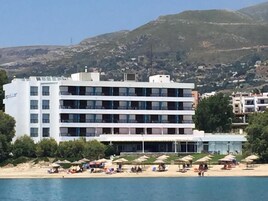 Un hotel de varios pisos, una playa con sombrillas y montañas al fondo.