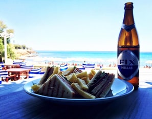 A plate of sandwiches and fries with a bottle of beer on a table by the beach. - Apollon Suite (Karystos)