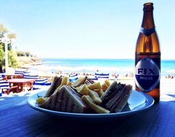 Un plato de sándwiches y papas fritas con una botella de cerveza sobre una mesa cerca de la playa.