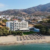 Un hotel frente al mar con varios pisos, piscina y playa con sombrillas.