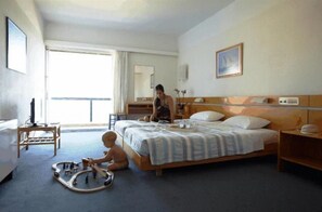 A hotel room with a bed, bedside table, and a child playing with toys. - Apollon Suite (Karystos)