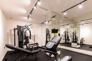 Un gimnasio con equipamiento de ejercicio, una banca y un espejo grande.