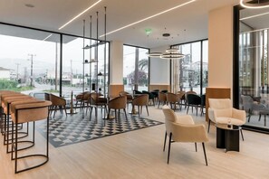 A modern interior with a mix of bar stools and chairs, a checkered floor, and large windows offering a view of the outside. - Canadian Annex (Zakynthos)