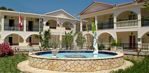 A hotel courtyard with a fountain, multiple balconies, and flags. - Canadian Annex (Zakynthos)