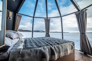 A room with a bed, a view of a snowy landscape through large windows, and curtains.